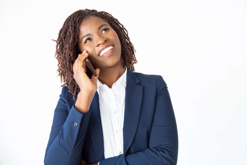 Smiling excited professional talking on mobile phone, looking at copy space. Young African American business woman standing isolated over white background. Communication concept